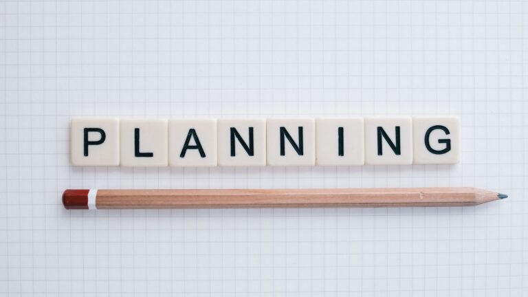 Overhead shot of letter tiles spelling 'planning' with a pencil on graph paper.
