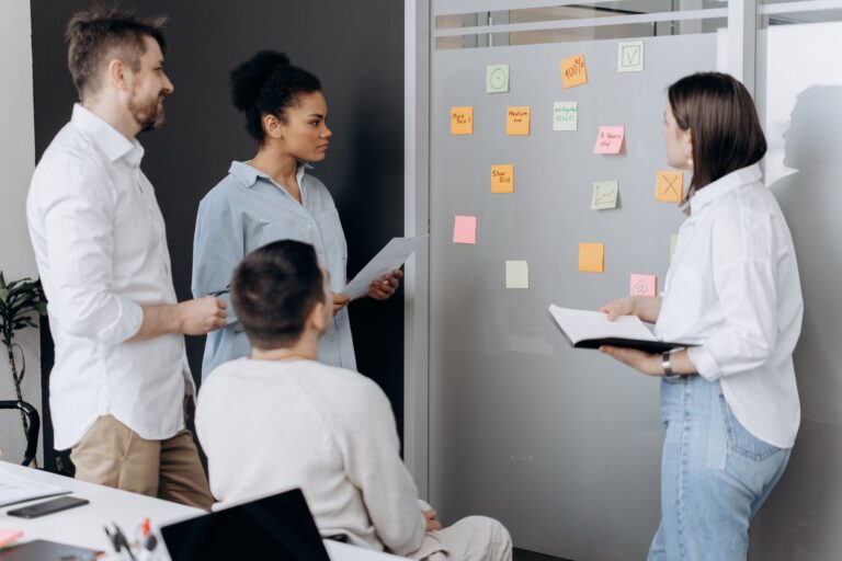 Diverse team collaborating in an office, discussing ideas using sticky notes and notepads.