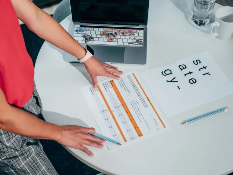 Top view of a person strategizing with documents and a laptop on a table.